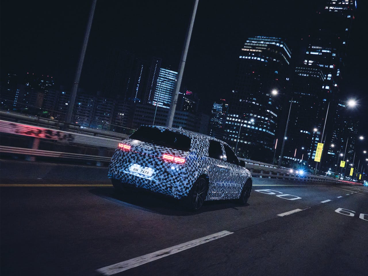 Mastering the First Impression: Your intriguing post title goes here Electric vehicle with camo wrap driving through illuminated city at night, showcasing futuristic car design.